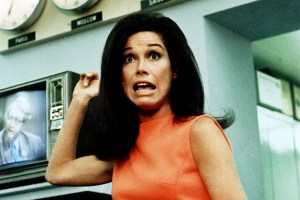 American actress and commediene Mary Tyler Moore, wearing a belted and sleeveless orange dress, worriedly points to an array of wall-mounted clocks in a scene from 'Mary Tyler Moore,' 1970. Moore plays Mary Richards, a woman who works in the newsroom of a television station. (Photo by CBS Photo Archive/Getty Images)